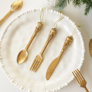 Detail of vintage gold cutlery Christmas tree ornaments on white plate with pine needles