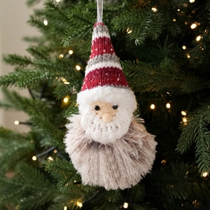 Knitted Santa plush ornament with red and white wool hat on glowing Christmas tree