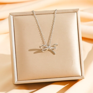 Collier élégant avec pendentif nœud argenté et zircons sur fond de soie luxueuse