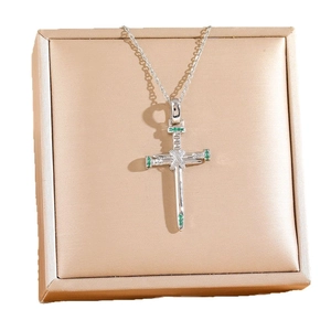 Elegant nail cross pendant necklace with green stones on a gold jewelry box