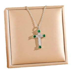 Silver cross necklace with green heart-shaped zircons on a luxury satin jewelry box