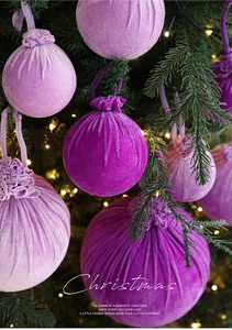 Detail of purple velvet Christmas ornaments with fine texture hanging on a lit tree
