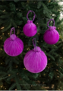 Close-up of purple velvet Christmas ball ornaments with texture hanging on a glowing tree