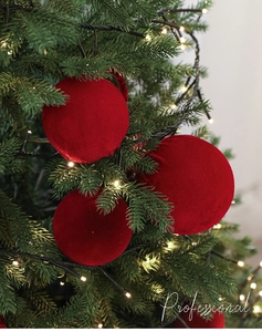 Detail of red velvet flocked Christmas ball with hanging loop on a lit Christmas tree