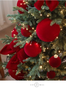 Detail of red flocked Christmas balls and velvet bow on tree with warm lights