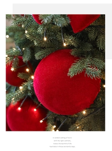 Close-up of red flocked Christmas ball ornament hanging on festive tree with warm lights