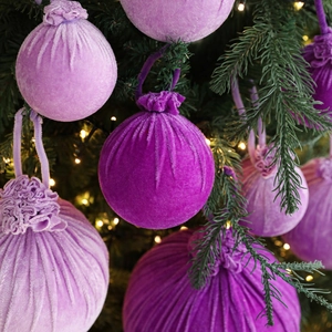 Purple flocked velvet Christmas ball ornaments hanging on a warm lit festive tree