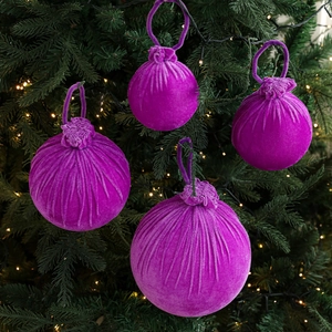 Set of four luxury purple velvet Christmas ball ornaments hanging on a festive green tree
