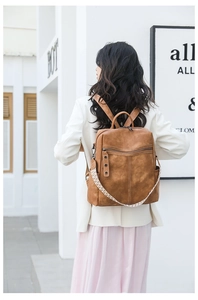 Detail view of caramel brown leather backpack with textured strap and front zipper pocket