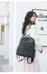 Close-up of black leather backpack with white contrast stitching and geometric strap