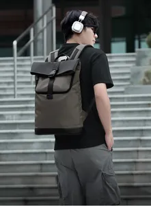 Side view of olive green roll-top backpack with black leather details on urban stairs