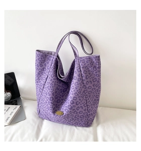 Detail of purple leopard print canvas tote bag featuring an oval gold metal logo plate