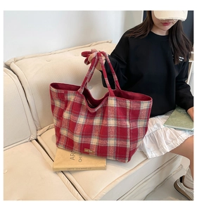 Detail of red and beige checkered wool tote bag with large capacity on a cream sofa