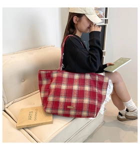 Detail shot of a large wool plaid tote bag with red patterns and a leather logo label