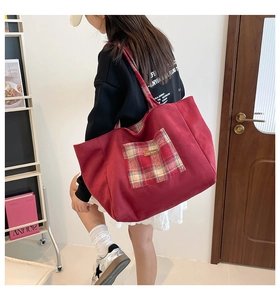 Detail of red canvas tote bag featuring a checkered front pocket and leather label