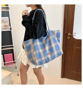 Detail of blue plaid wool tote bag with leather logo patch shown on a model