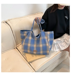 Close-up of blue plaid tote bag with brown leather label and double handle details