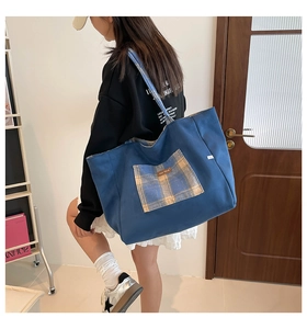 Detail of blue canvas tote bag featuring a yellow plaid pocket and wide shoulder strap