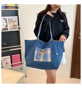 Close-up of the blue canvas tote bag featuring a yellow plaid pocket and leather patch