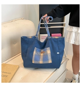Detail of blue canvas tote bag with plaid pocket and woven straps in a cozy room