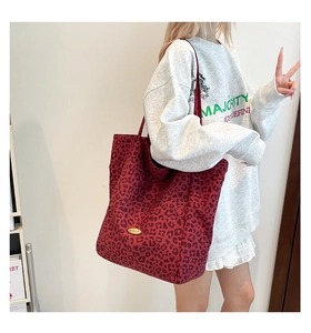 Detail showing the red leopard print canvas tote bag with a gold metal brand plate