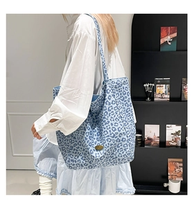 Close-up of a blue leopard print tote bag with a gold metal emblem on a model