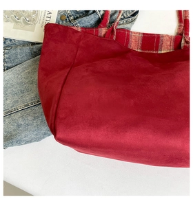 Detail of red suede tote bag with British plaid lining on denim and magazine background