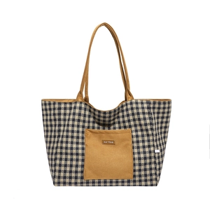 Detail of grid patterned canvas tote bag featuring brown front pocket and logo label