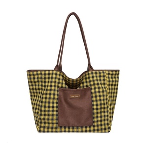 Detail of a large canvas plaid tote bag with brown shoulder straps and outer pocket