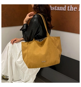 Close-up of a large mustard canvas tote bag with metal nameplate shown on model