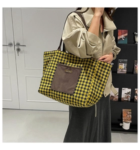 Detailed view of a yellow plaid canvas tote bag with a brown front pocket worn by a model
