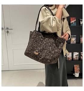 Detail of leopard print canvas tote bag featuring brown leather logo patch on surface