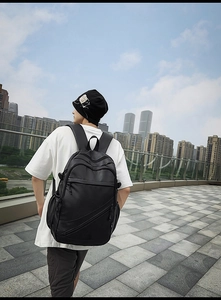 Back view of a large black faux leather backpack for men in an urban setting.