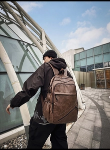 Side view of dark brown vintage leather backpack worn by a man in a modern street setting