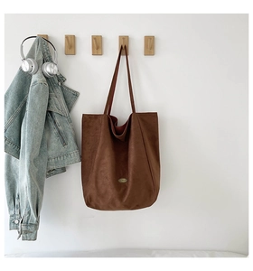 Detail of a large dark brown suede tote bag hanging on a wooden hook with headphones