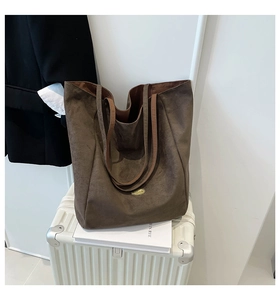 Detail of matte faux suede tote bag with golden logo plaque on white suitcase