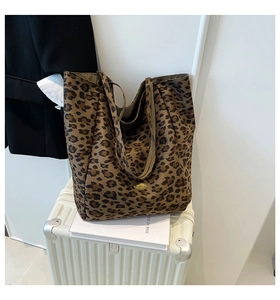 Detail of leopard print tote bag with gold metal logo on a white suitcase background