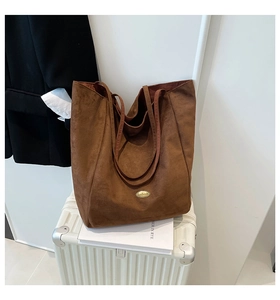 Close-up of brown suede tote bag with handmade metal logo on a white suitcase