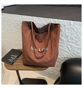 Detail view of the waterproof caramel brown tote bag with white MALIVI text on a wood table