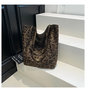 Close-up of leopard print canvas tote bag with gold logo plaque on a minimalist display