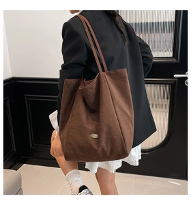 Detail view of large brown suede tote bag with metallic logo on textured fabric