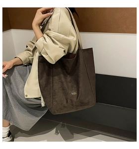 Detail of a dark brown suede tote bag with a metallic logo on a shoulder-carried model