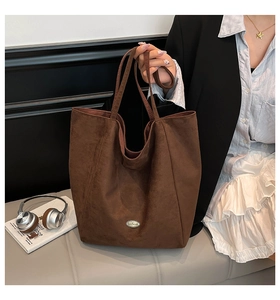 Detail of dark brown suede tote bag featuring a handmade metal logo and long shoulder straps