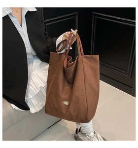 Detail of soft brown suede tote bag with dual handles and metal logo plate shown in use
