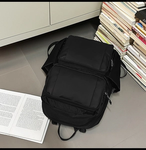 Top view of a black nylon backpack with multi-zipper pockets among stack of books