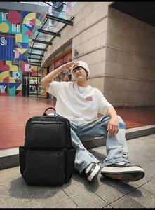 Black multi-pocket commuter backpack shown in a lifestyle outdoor setting with model