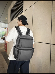 Dark grey large capacity backpack with wide padded straps on a model in urban setting