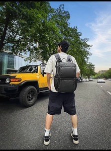 Outdoor view of a black business backpack on a man's back featuring multiple zip pockets