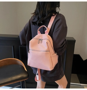 Détail d'un sac à dos rose clair avec texture tissée et zips argentés porté par le mannequin