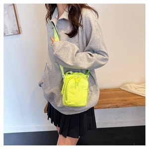 Detail of neon yellow crossbody phone bag with wide strap worn by a female model